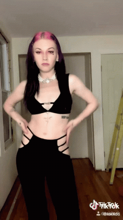 Woman With Purple Hair And Tattoo Standing In Hallway Hands On Hips GIF