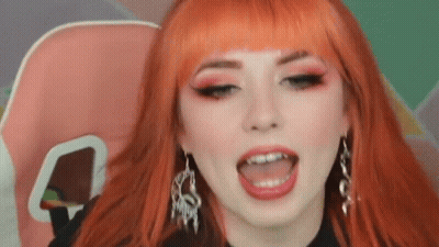Woman With Red Hair And Earrings Sitting With Tongue Out GIF
