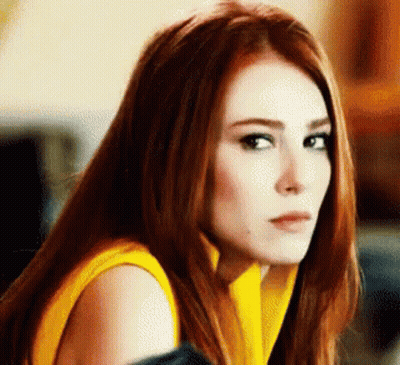 Woman With Red Hair In Yellow Sweater Looking At Camera GIF