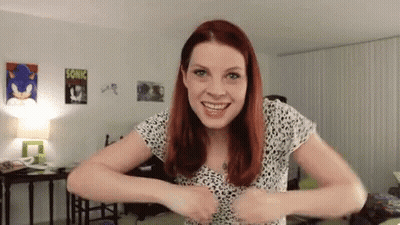 Woman With Red Hair Standing In Living Room Hands On Chest GIF