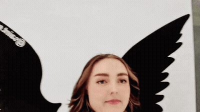 Woman With Scarf Standing In Front Of Bird Wings Painting GIF