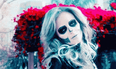 Woman With Skeleton Makeup Sitting In Front Of Flowers GIF
