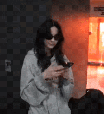 Woman With Sunglasses Looking At Phone In Dark Room GIF