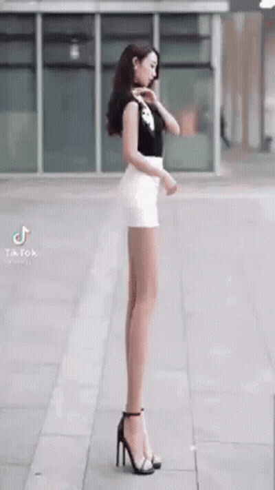 Woman With Very Long Legs On Sidewalk In Heels GIF