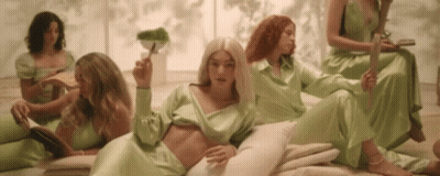 Women In Green Dresses Around Laying Woman GIF