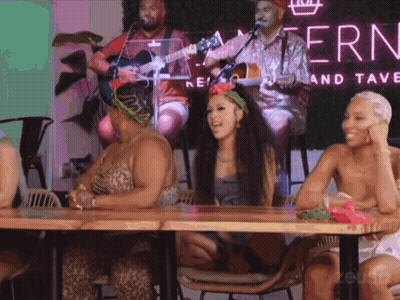 Women Sitting At Table In Front Of Fern Sign GIF