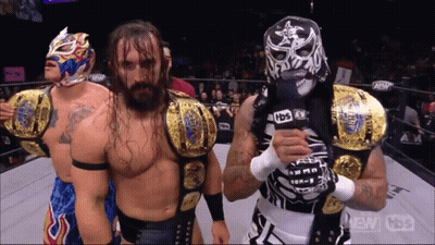 Wrestler In Mask Holding Microphone With Two Wrestlers GIF
