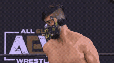 Wrestler In Mask In Front Of All Elite Wrestling Sign GIF