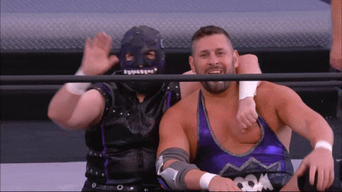 Wrestler In Mask Sitting Next To Purple Tank Top GIF