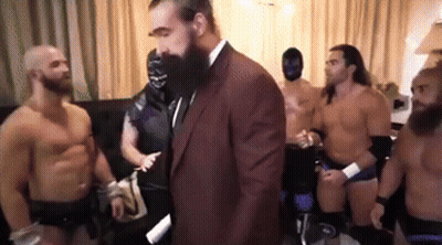 Wrestlers Standing Around Man In Suit And Tie GIF