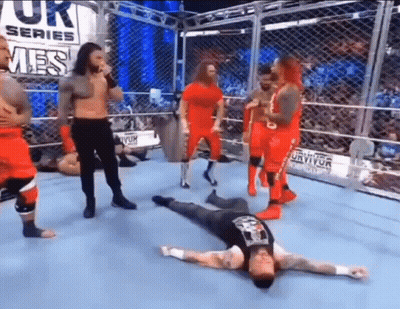 Wrestlers Standing Around Man Laying On Floor GIF