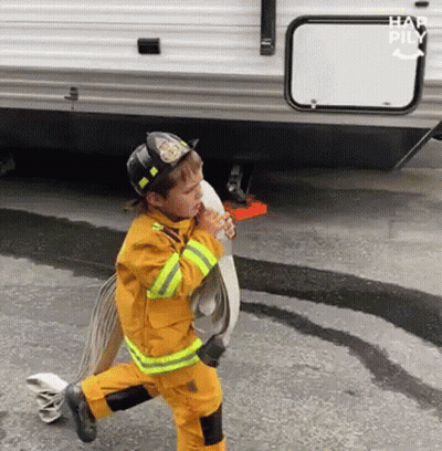 Young Boy Dressed As Firefighter Holding Fire Hose GIF