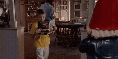 Young Boy Holding Book Next To Santa Claus Statue GIF