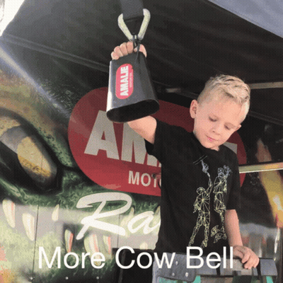 Young Boy Holding Cow Bell In Front Of More Cow Bell Sign GIF