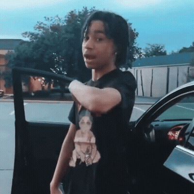 Young Boy In Black T-Shirt Standing In Front Of Car GIF