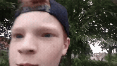 Young Boy In Blue Hat Standing In Front Of Trees GIF