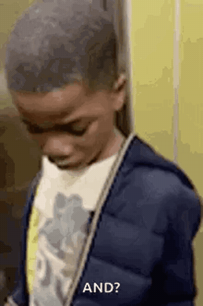 Young Boy In Blue Jacket Looking Down Against Yellow Wall GIF