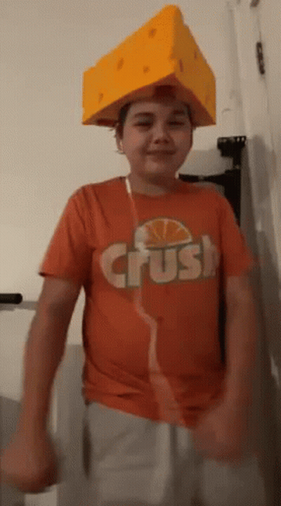 Young Boy In Orange Shirt And Cheese Hat Dancing GIF