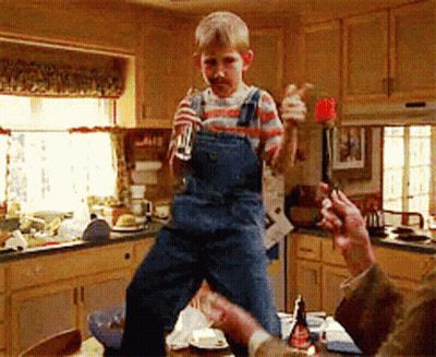 Young Boy In Overalls Standing On Table Holding Glass GIF