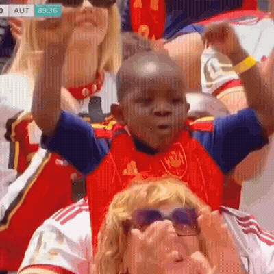 Young Boy In Red And Blue Adidas Shirt Sitting In Crowd GIF