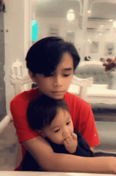 Young Boy In Red Shirt Holding Baby GIF
