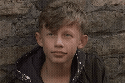 Young Boy Leaning Against Stone Wall Looking At Camera GIF