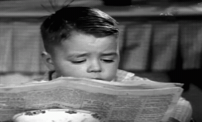 Young Boy Reading Newspaper At Table GIF