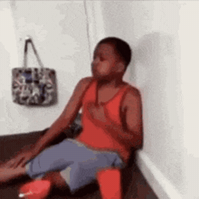 Young Boy Sitting On Floor Next To Wall And Purse GIF