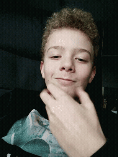 Young Boy With Curly Hair Making Face With Hand GIF