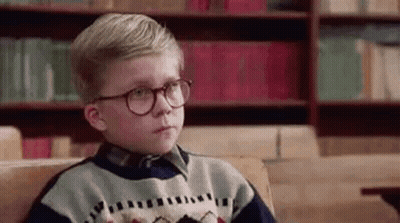 Young Boy With Glasses Sitting On Couch In Front Of Bookshelf GIF