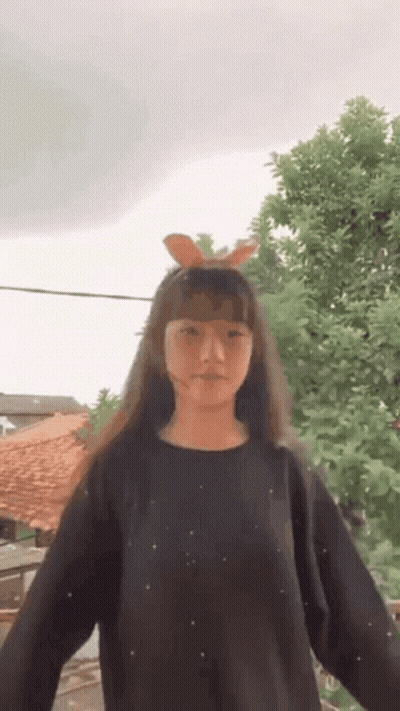 Young Girl In Black Sweater With Bunny Ears Standing In Front Of Tree GIF
