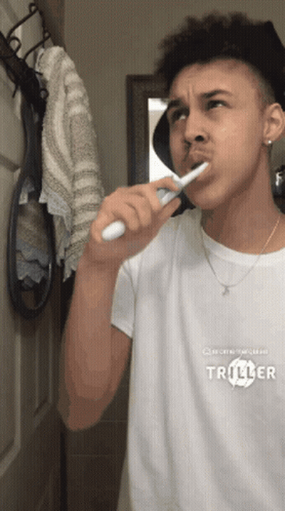 Young Man Brushing Teeth In Mirror Wearing Triller Shirt GIF