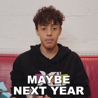 Young Man Curly Hair Sitting In Front Of Maybe Next Year Sign GIF