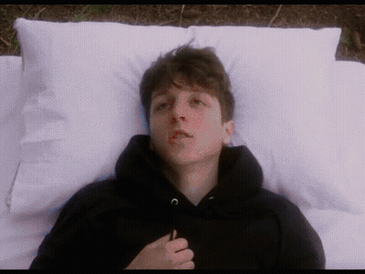 Young Man In Black Hoodie Laying On Bed With White Pillows GIF