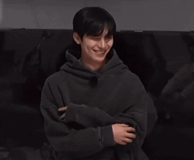 Young Man In Black Hoodie Sitting On Couch Holding Cell Phone GIF