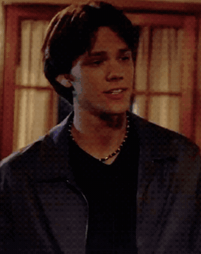 Young Man In Black Shirt And Blue Jacket At Window GIF