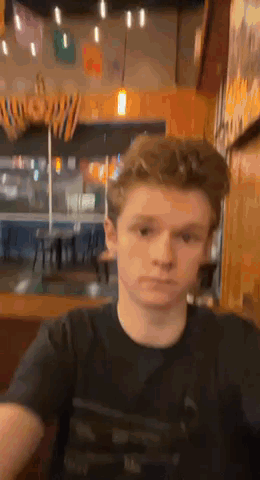 Young Man In Black T-Shirt Sitting In Restaurant GIF