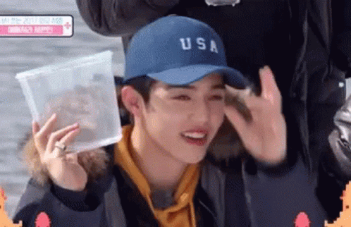 Young Man In Blue Hat Holding Plastic Container GIF