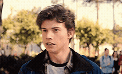 Young Man In Blue Jacket And Plaid Shirt Standing By Trees GIF