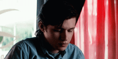 Young Man In Blue Shirt Sitting At Table With Red Curtain GIF