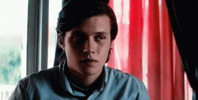 Young Man In Blue Shirt Sitting By Window With Red Curtain GIF