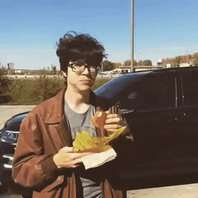 Young Man In Brown Jacket Eating Sandwich GIF