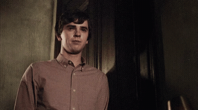 Young Man In Brown Shirt Standing In Dark Room GIF