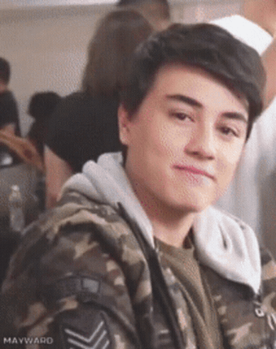 Young Man In Camouflage Jacket Sitting In Crowd GIF