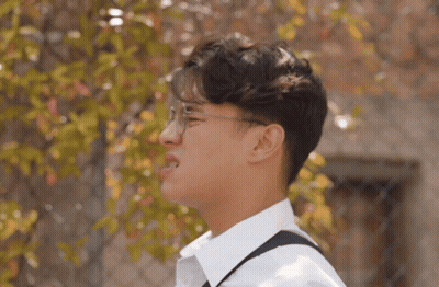 Young Man In Glasses And White Shirt Standing By Fence GIF