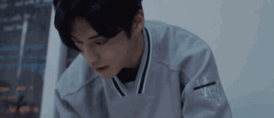 Young Man In Gray Sweater Sitting At Table In Dark Room GIF