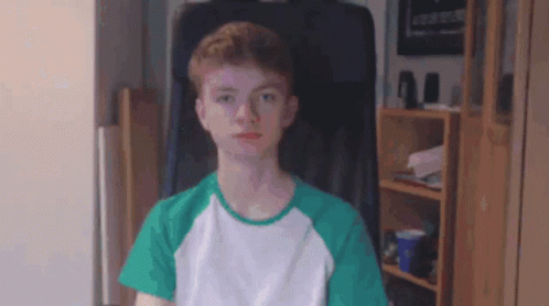 Young Man In Green And White Shirt Sitting In Chair GIF