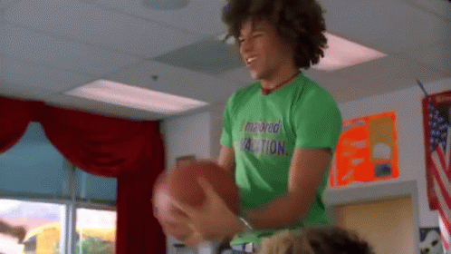 Young Man In Green Shirt Holding Football In Classroom GIF