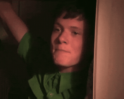 Young Man In Green Shirt Looking Out Doorway GIF