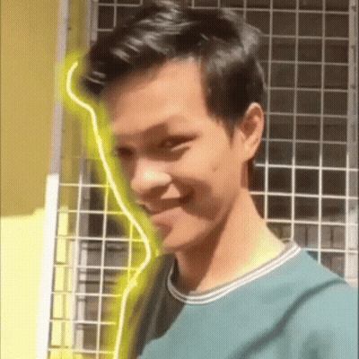Young Man In Green Shirt Smiling In Front Of Yellow Light GIF